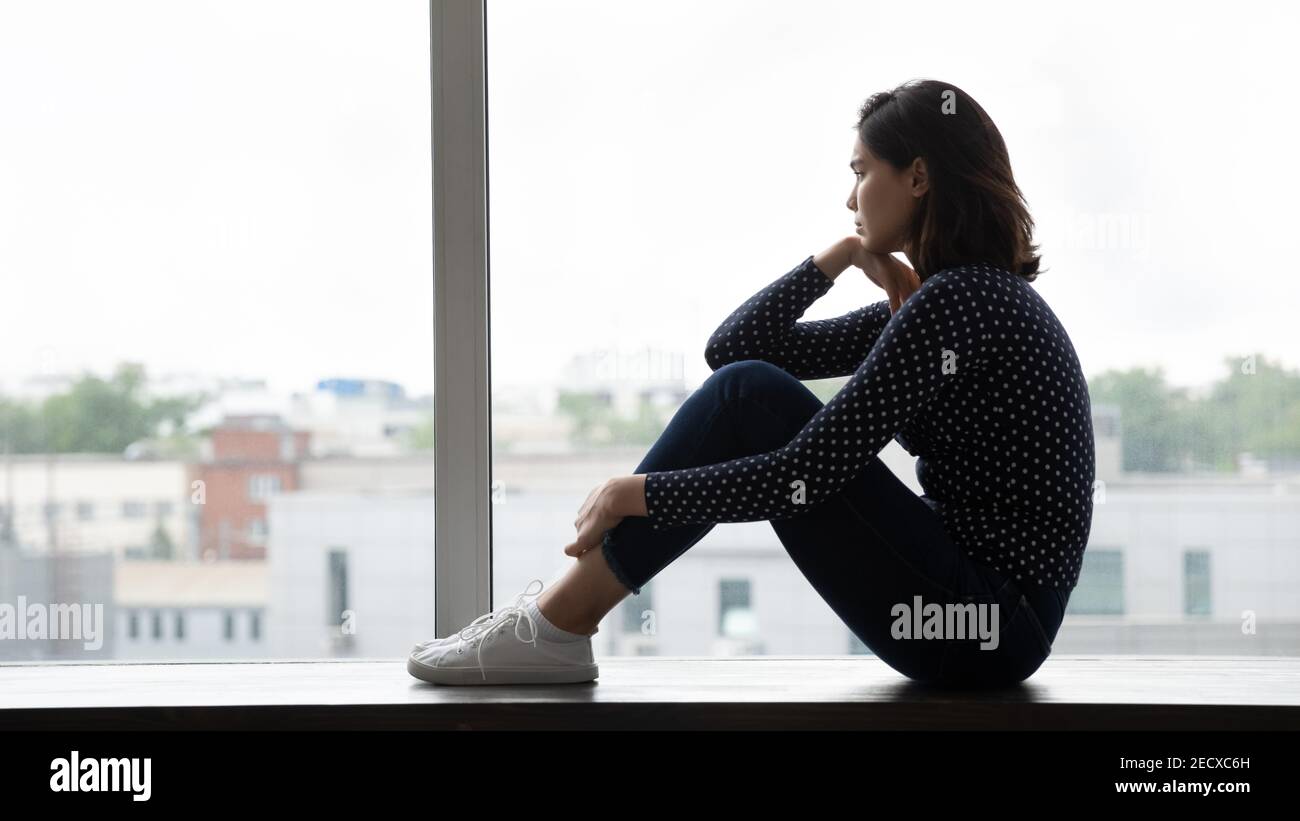 Junge asiatische Frau sitzen auf Fenster Umarmung Knie wegschauen Stockfoto