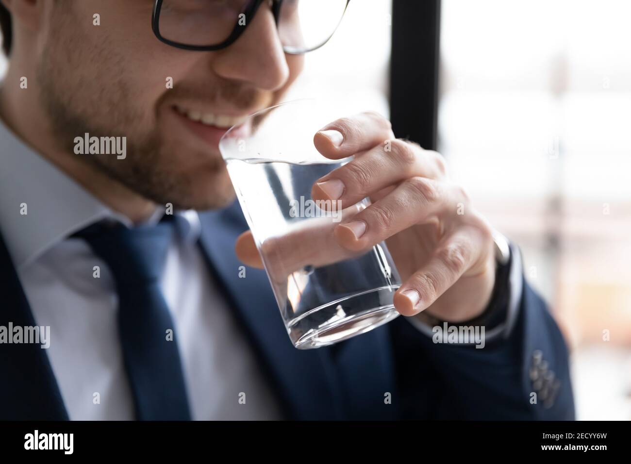 Lächelnder Mann trinkt reines Mineralwasser aus Glas Stockfoto