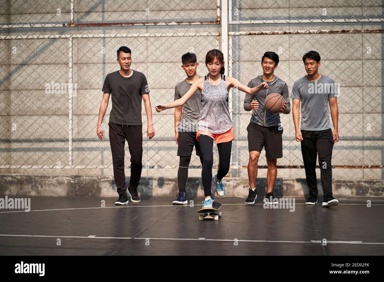 Junge asiatische Frau Skateboarder Skateboarding im Freien mit Freunden beobachten von hinten Stockfoto