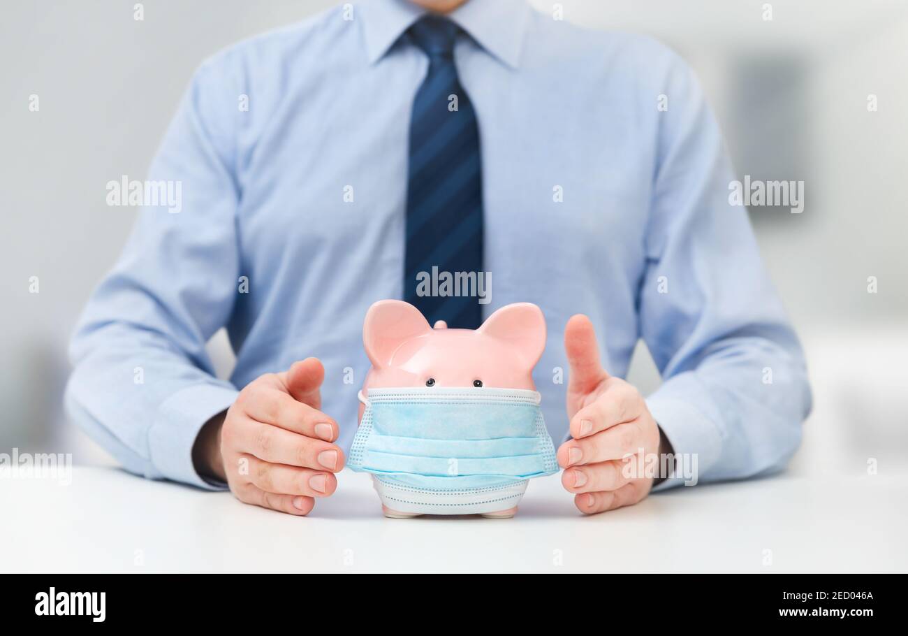 Geschäftsmann hält Sparschwein mit Maske. Finanzielle Probleme von Unternehmern während des Pandemiekonzepts Stockfoto