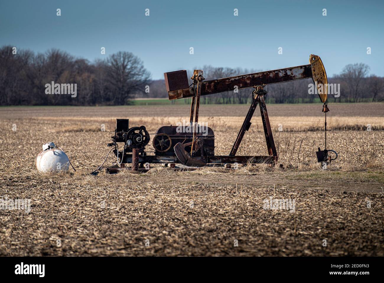 Ein alter rostiger Ölpumpenheber mit Stützausrüstung sitzt in geerntetem Maisfeld im amerikanischen Mittleren Westen, wo Landwirte Pumpen auf ihrem Grundstück haben können. Stockfoto