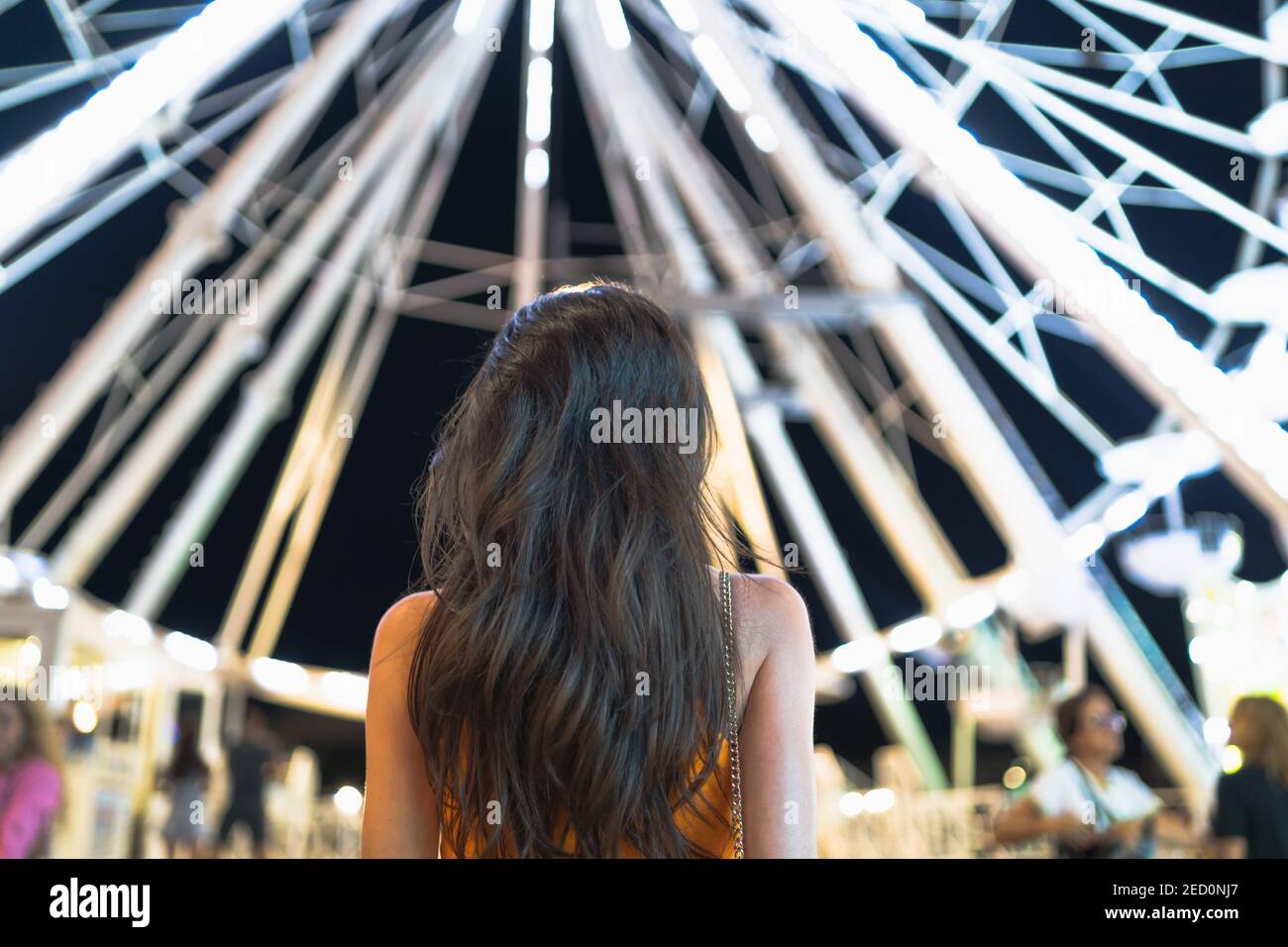 Rückansicht einer Frau mit langen braunen Haaren Das Riesenrad leuchtet in der Nacht Stockfoto