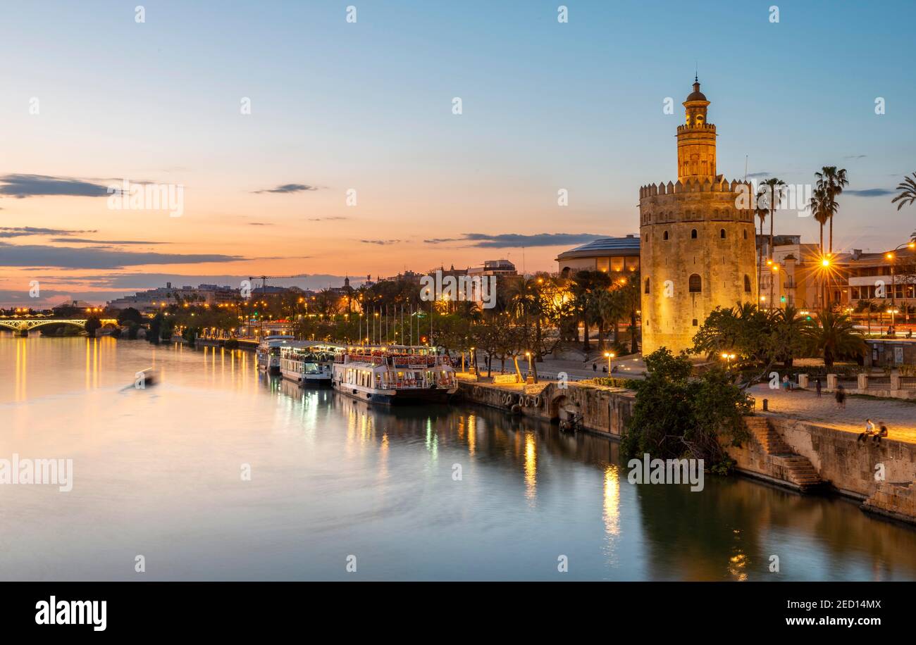 Blick über den Fluss Rio Guadalquivir mit Torre del Oro und Promenade mit Ausflugsbooten, Sonnenuntergang, blaue Stunde, Sevilla, Andalusien, Spanien Stockfoto