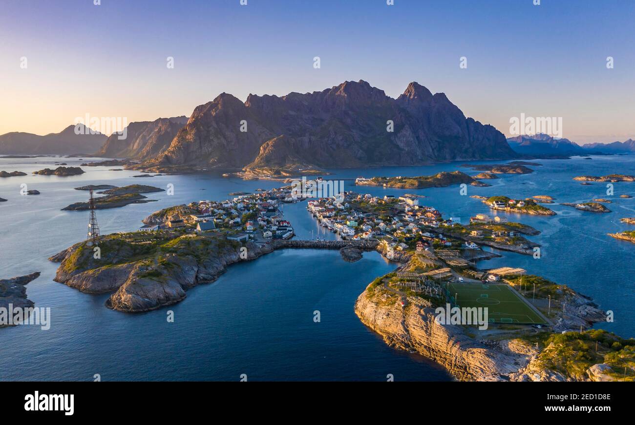 Luftaufnahme, Abendsonne über Henningsvaer mit Fußballstadion, Felseninseln im Meer vor Bergen, Festvagtinden, Vestvavoy, Lofoten, Nordland Stockfoto