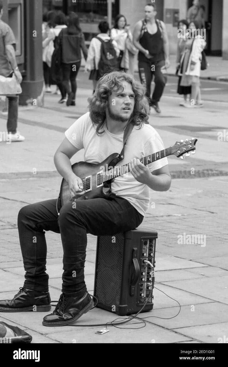 Mitten im Stadtzentrum von York saß ein Mann mit langen, lockigen Haaren auf einem kleinen Lautsprecher und spielte eine elektrische Gitarre., North Yorkshire, Großbritannien. Stockfoto