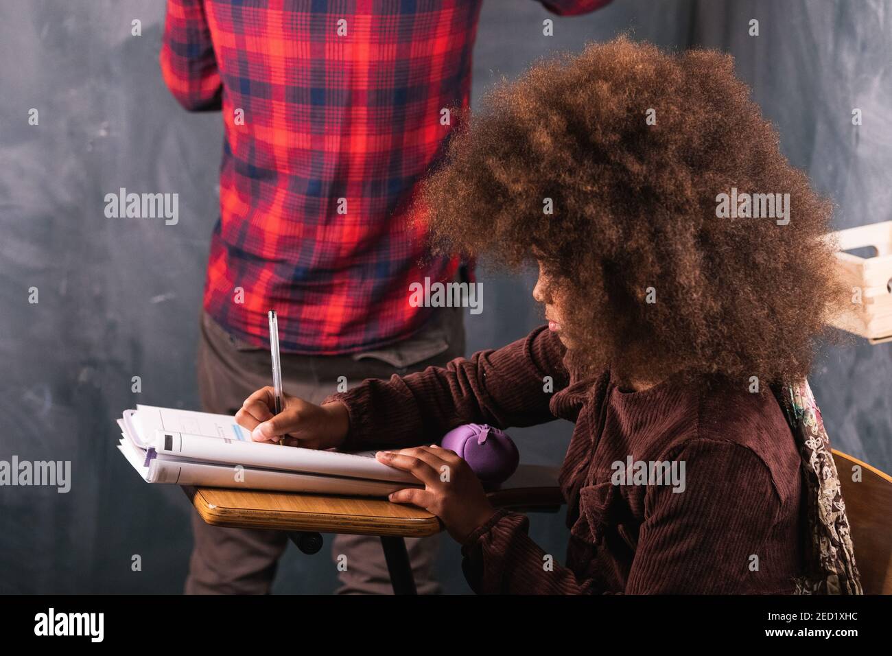 Zugeschnittenes unerkennbarer Lehrer Schreiben mathematisches Beispiel auf Kreidetafel für schwarz Mädchen sitzt am Schreibtisch im Klassenzimmer während des Unterrichts in der Schule Stockfoto