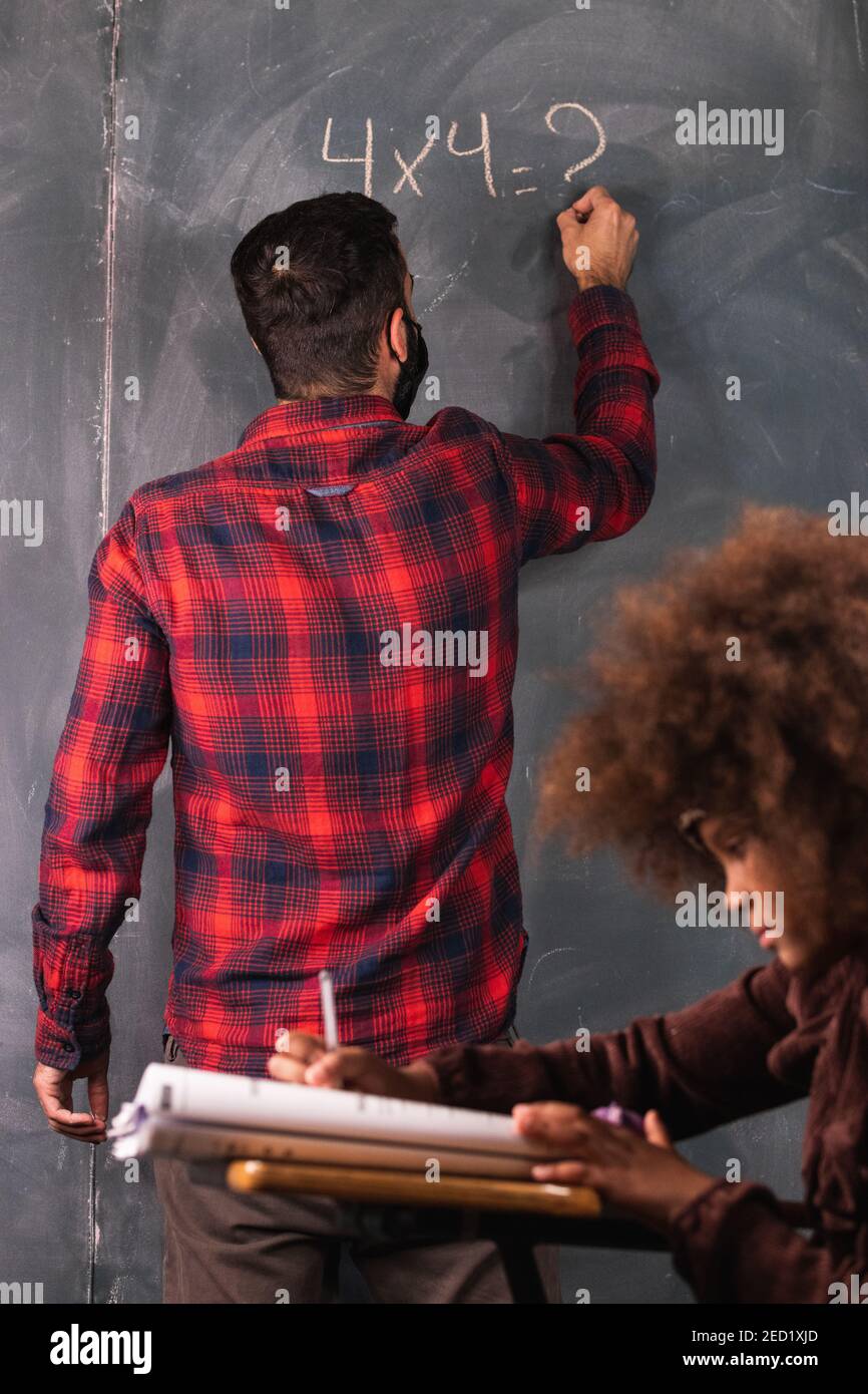 Lehrer schreiben mathematische Beispiel auf Kreidetafel für schwarze Mädchen sitzen Am Schreibtisch im Klassenzimmer während des Unterrichts in der Schule Stockfoto
