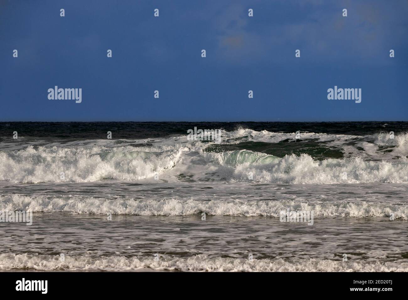 WINTERSZENE DUNKELBLAUER HIMMEL UND GRÜNE WELLEN MIT SCHAUM UND SPRAY KRACHEND AUF EINEN STRAND Stockfoto