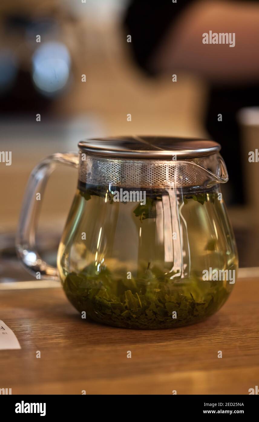 Nahaufnahme des Teekessel-Servers aus Glas mit grünem Tee auf dem Tisch im Café mit verschwommenem Hintergrund, niemand Stockfoto