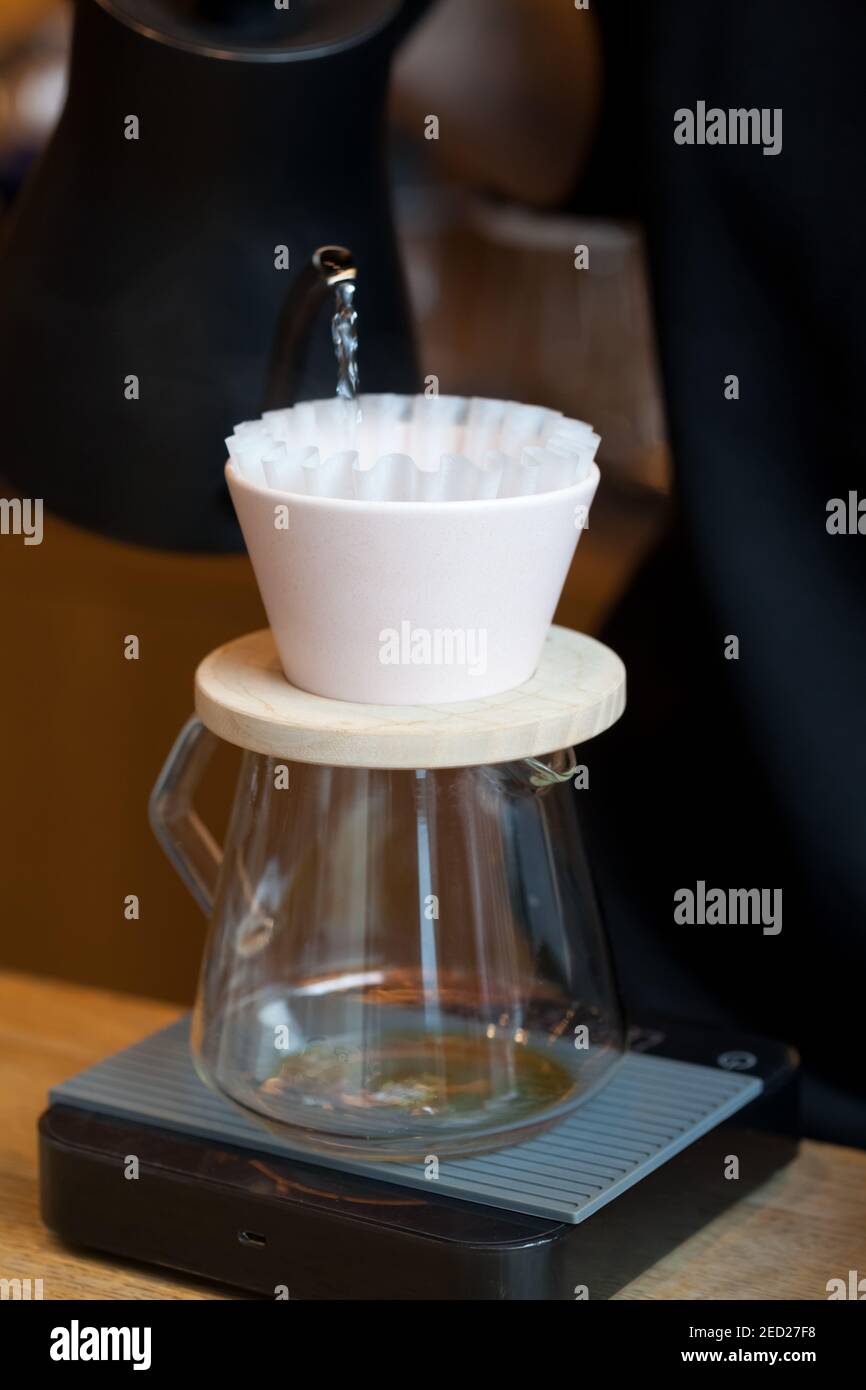 Barista gießt Wasser aus dem Wasserkocher in kalita gießen mit Papierfilter auf Digitalwaagen Stockfoto