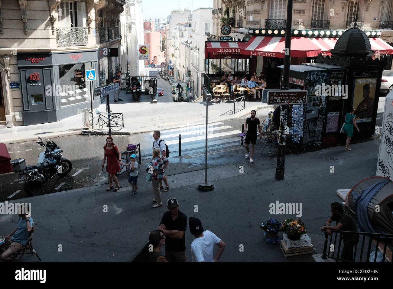MONTMARTRE, PARIS - 29th. JUNI 2019: Eine geschäftige Pariser Straße in der Rue Lamarck Szene im 18th Arrondissement. Im Café La Refuge sitzen Einheimische in der Sonne. Stockfoto