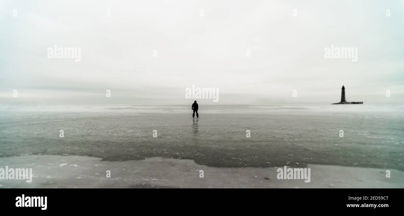 Silhouette eines einsamen Mannes und eines Leuchtturms auf Eis In gefrorenem Meer Blick nach hinten Stockfoto