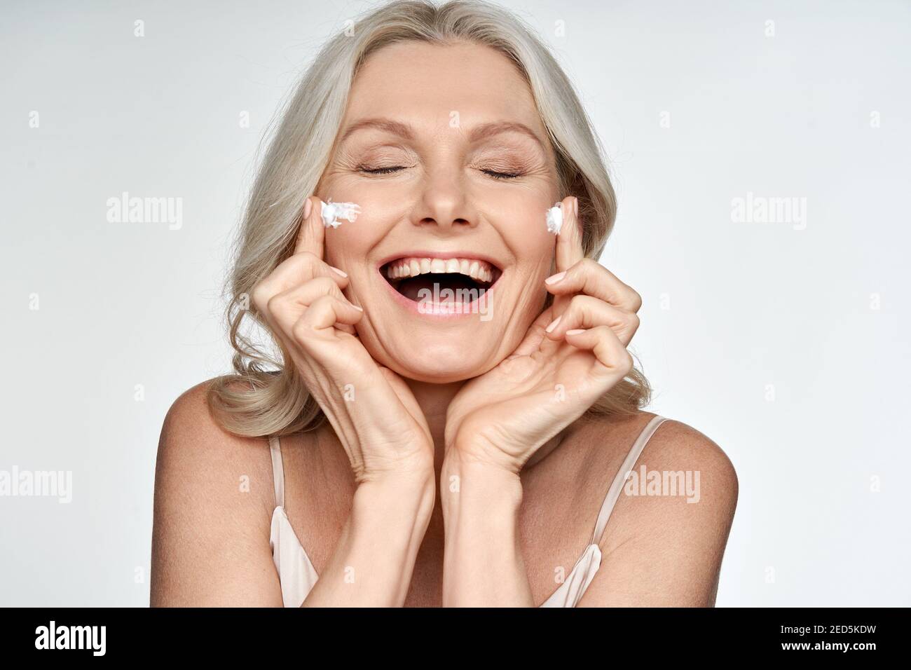 Glücklich lustige 50s Frau mittleren Alters Anwendung Creme auf Gesicht isoliert auf weiß. Stockfoto