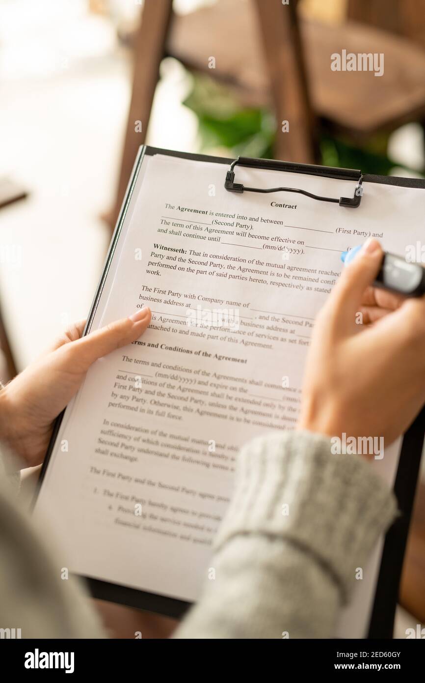 Hände der jungen Bewerberin mit blauem Textmarker über Vertrag In der Zwischenablage Text nach dem Interview mit dem Arbeitgeber vor der Unterzeichnung zu lesen IT Stockfoto