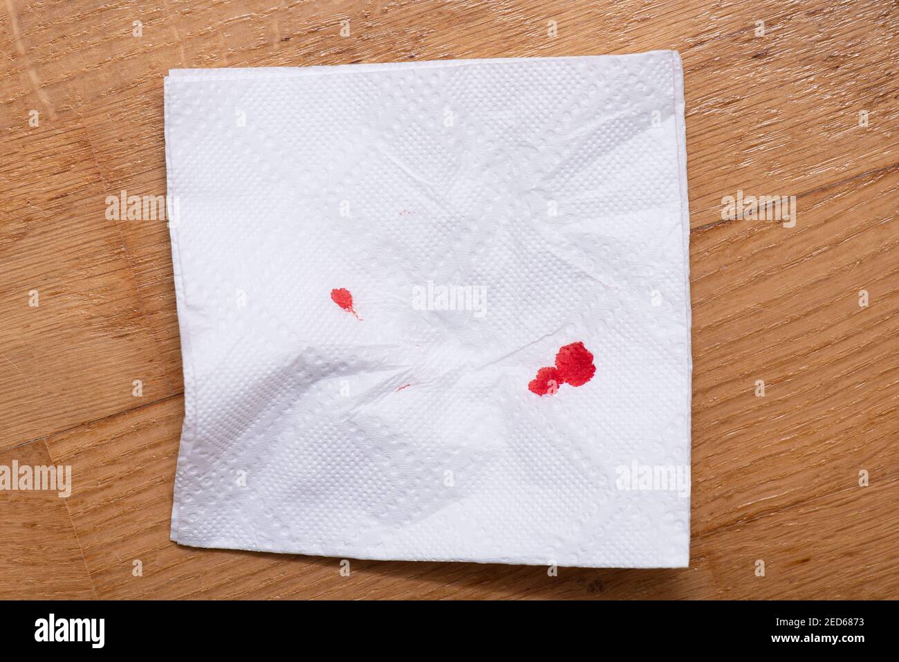 Tropfen von echtem Blut auf zerknitterter Papierserviette. Blutige Serviette auf Holzboden. Stockfoto