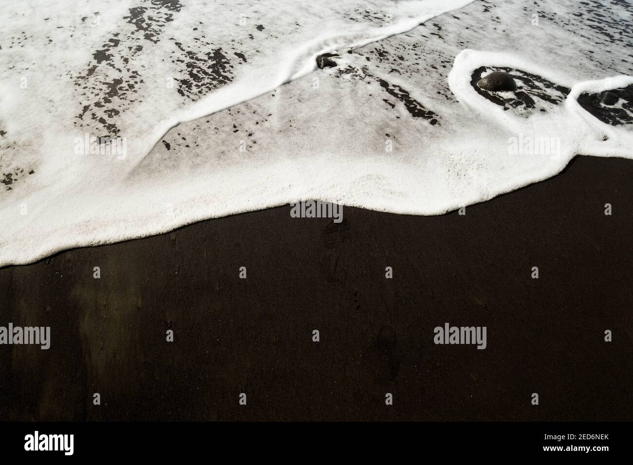 Weiße Brandung, die über schwarzen vulkanischen Sand fließt. Keine Personen. Speicherplatz kopieren. Stockfoto