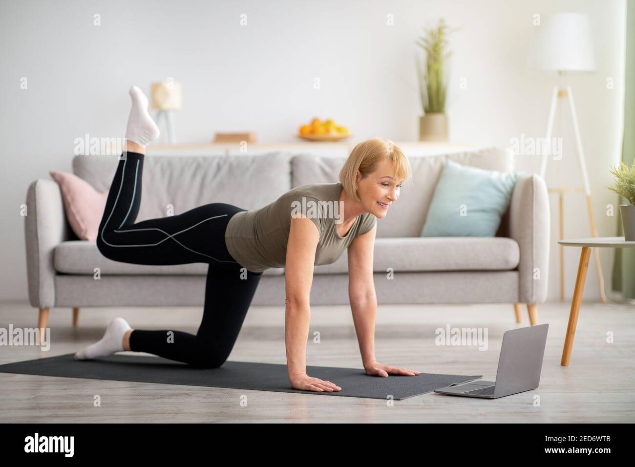 Online Home Fitness-Konzept. Schöne reife Frau Ausübung zu Sport-Video auf Laptop im Wohnzimmer Stockfoto