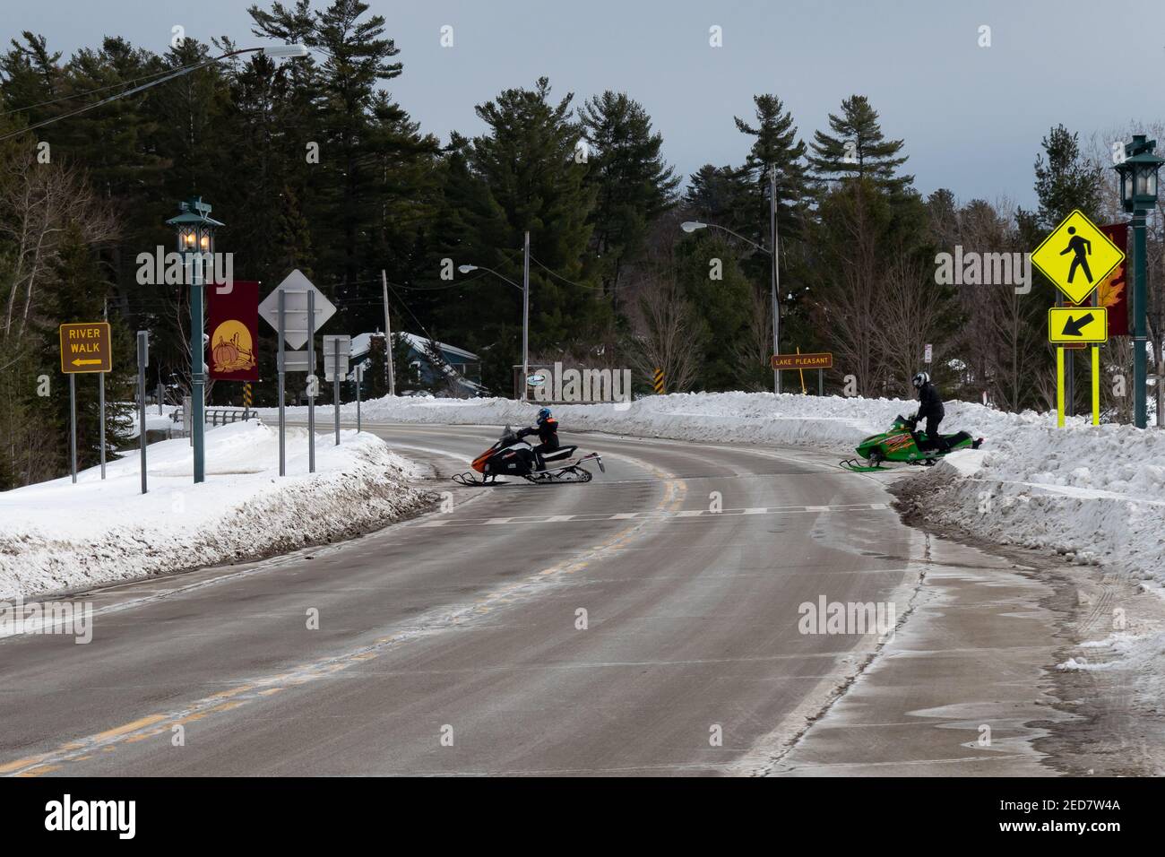 Zwei Schneemobile überqueren die Autobahn am Lake Pleasant in Speculator, NY an einem Winternachmittag. Stockfoto