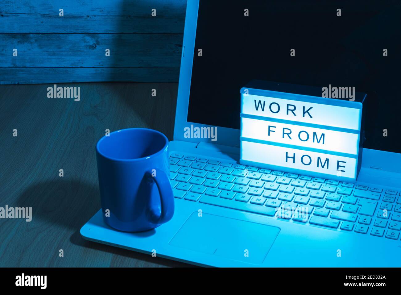Laptop-Computer und Kaffeetasse zusammen mit einem Leuchtkasten Anzeige der Arbeit von zu Hause aus soziale Fernarbeit in der Zeit covid19 Konzept Gesundheit mit bläulichem Licht Stockfoto