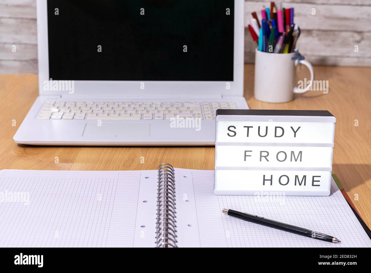 Selektiver Fokus eines Studientischs mit einem Notizbuch, Stiften und einem Laptop-Computer zusammen mit einem Leuchtkasten, der Home Study in covid19 Time Confineme anzeigt Stockfoto