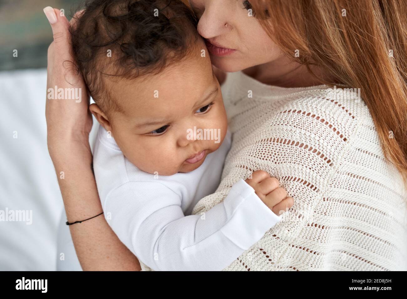 Liebevolle kaukasische Mutter umarmt niedlichen Säugling afroamerikanischen Baby Tochter. Stockfoto