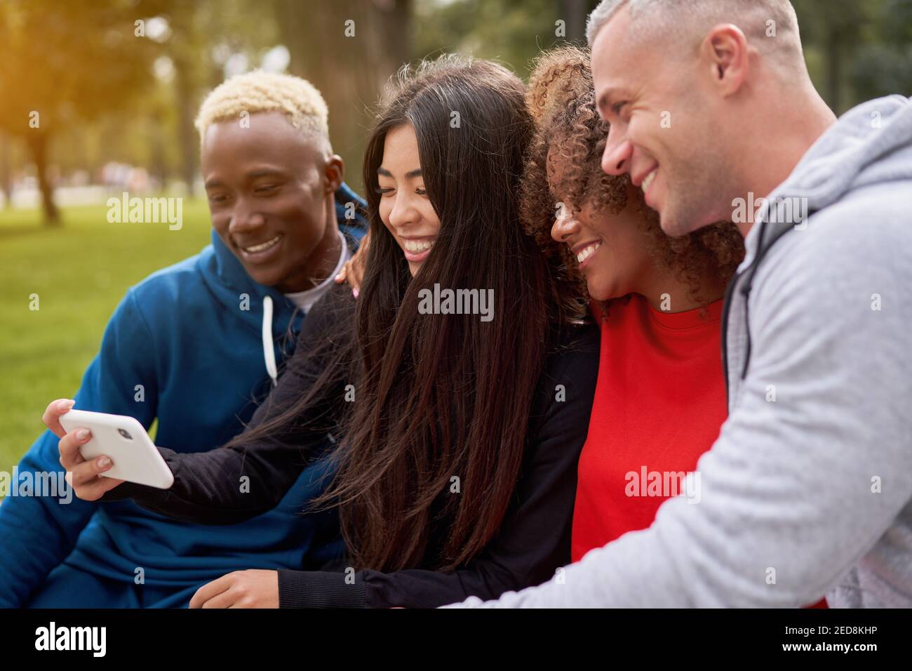 Multi ethnische Freunde im Freien suchen Smartphone-Bildschirm. Diverse Gruppe Menschen Afro american Asian kaukasischen verbringen Zeit zusammen multirassischen männlichen weiblichen Studenten Sitzbank Park im Freien Stockfoto