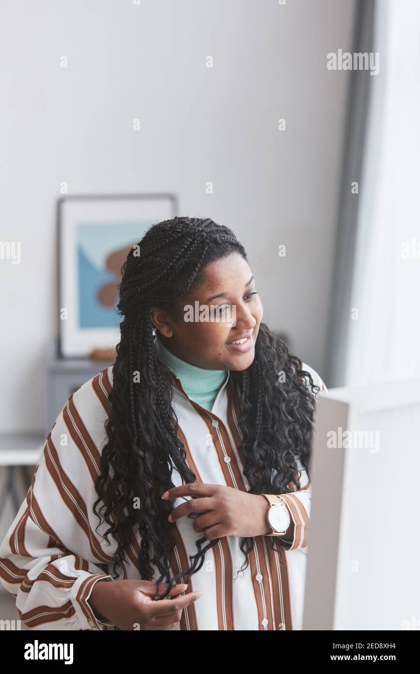 Vertikale Porträt von kurvigen afroamerikanischen Frau in Spiegel und Lächelnd, während Sie sich zu Hause verkleiden Stockfoto