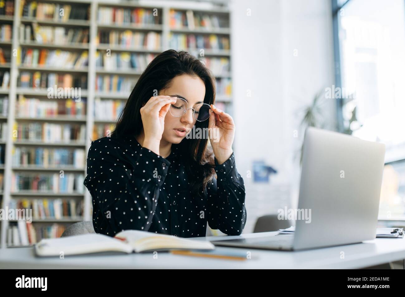 Kaukasische Studentin oder Mitarbeiterin in Brillen sitzt am Schreibtisch, müde von Online-Arbeit oder Studium. Erschöpfte Freiberuflerin Frau mit Kopfschmerzen, brauchen eine Pause Stockfoto