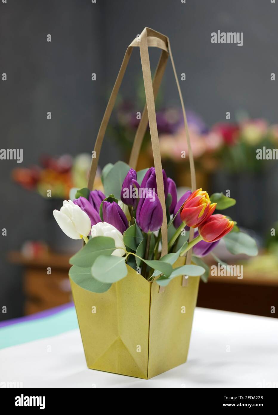 Ein Bouquet von Tulpen in einem dekorativen Papierkorb gegen Der Hintergrund von anderen Blumen in einem Dekor und Floristik Speichern Stockfoto
