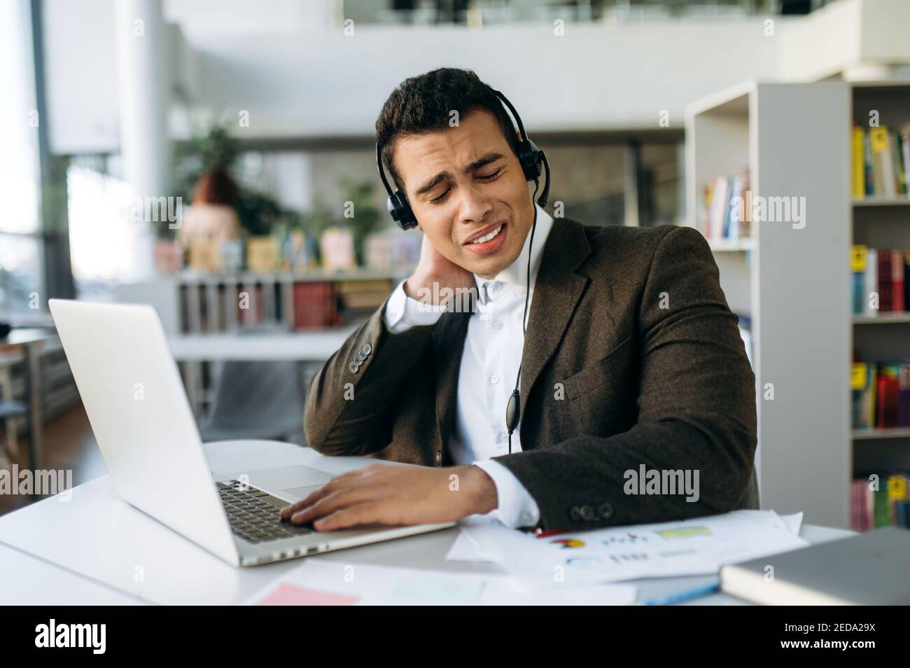 Der spanische Manager oder Callcenter-Mitarbeiter sitzt am Arbeitsplatz mit einem Headset und einem Laptop. Müder Programmierer oder Tutor arbeitet ohne Pause, haben Nackenschmerzen, brauchen eine Pause oder Pause Stockfoto