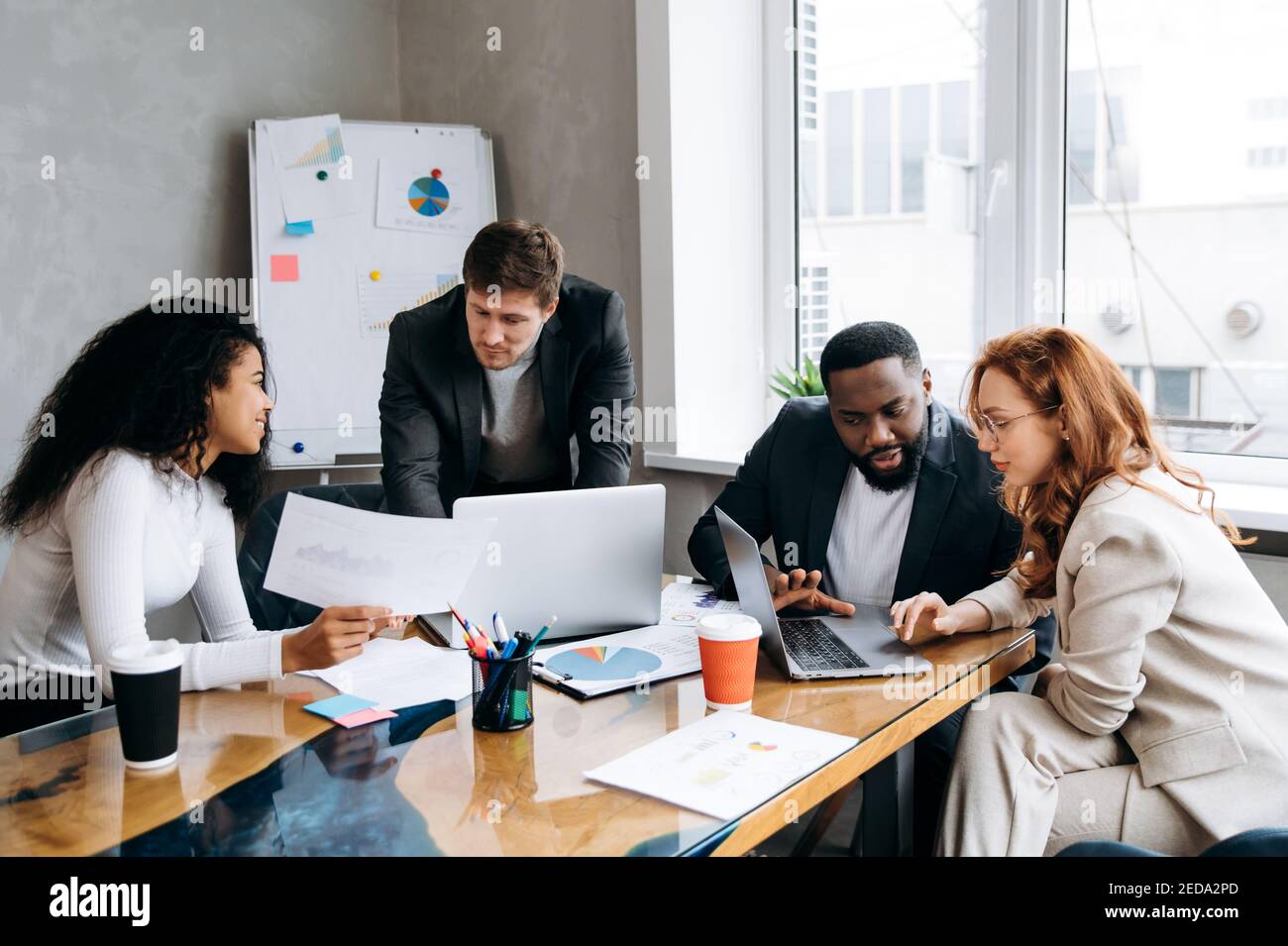 Business Briefing Meeting. Erfolgreiche Gruppe von Menschen, die Finanzdiagramme und Diagramme betrachten, Brainstorming zusammen. Multiethnische männliche und weibliche Mitarbeiter diskutieren Ideen, arbeiten an einem neuen Projekt Stockfoto