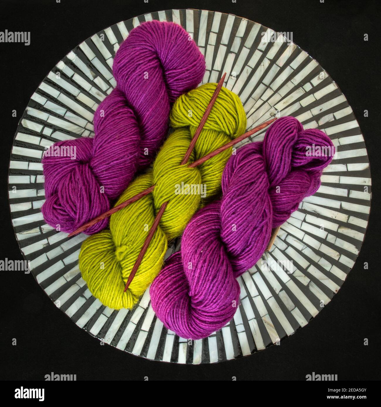Fuchsia und Chartreuse Garn mit Stricknadeln auf schwarz gekreuzt Und weißem Tisch Stockfoto