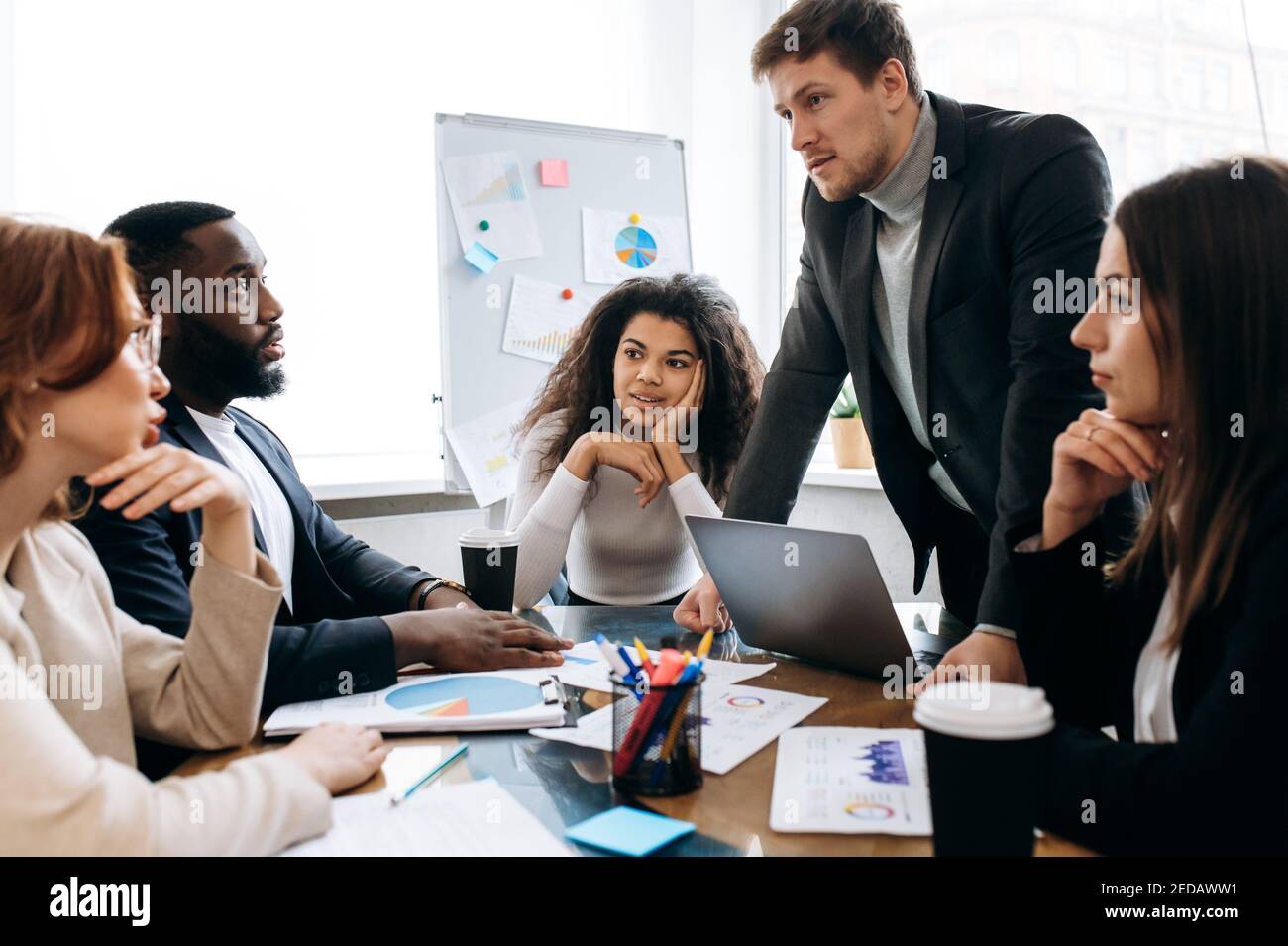 Fokussierte Kollegen in formeller Kleidung bei Verhandlungen. Multirassische männliche und weibliche Mitarbeiter diskutieren über Ideen für Projekt, Lernen Finanzgraphen. Business Partners Brainstorming zusammen Stockfoto