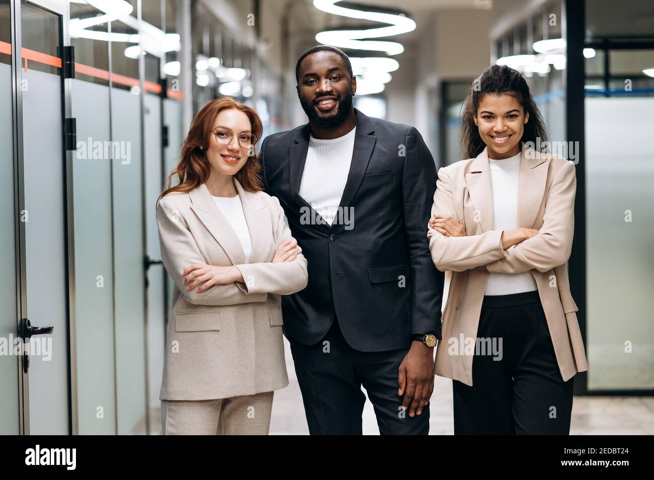 Multirassische einflussreiche Geschäftsleute in formeller Kleidung schauen lächelnd auf die Kamera. Glückliche weibliche und männliche Kollegen stehen im modernen Büro, zeigen Vertrauen und Erfolg, Teamwork-Konzept Stockfoto