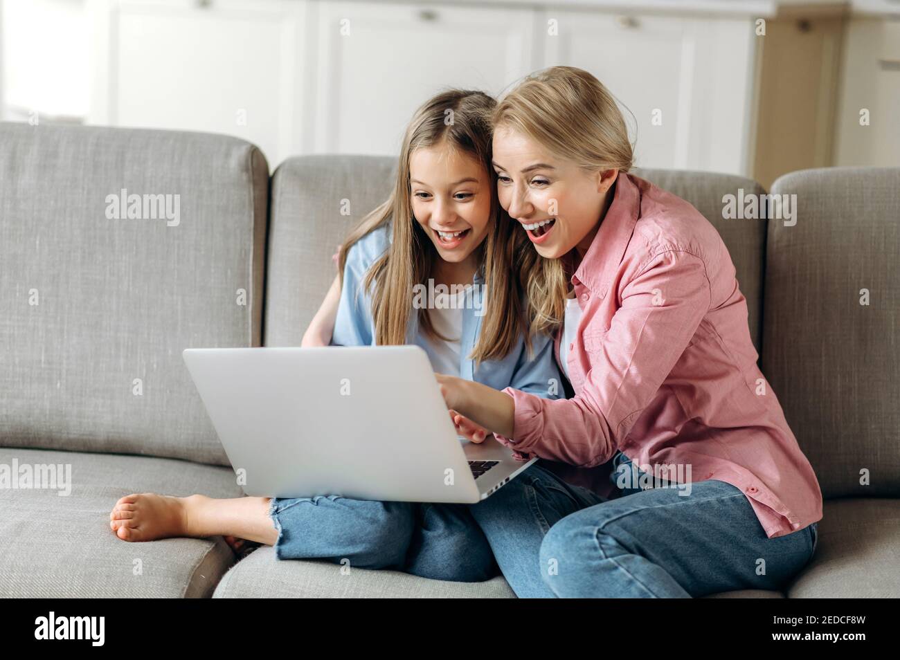 Freizeit von Mutter und Tochter. Glückliche kaukasische Mutter und Tochter sitzen auf der Couch, mit einem Laptop, lachen, im Internet surfen, online einkaufen, Gute Nachrichten Stockfoto