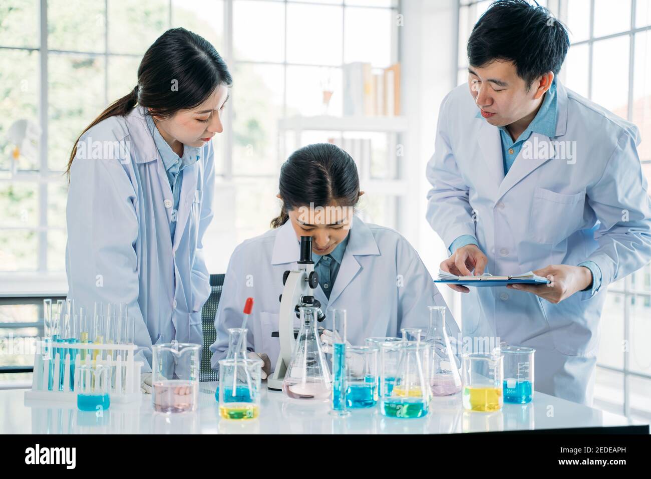 Gruppe junger asiatischer Wissenschaftler mit Labcoat Zusammenarbeit im Labor mit Mikroskop zu studieren und zu entwickeln Neuer Antivirenimpfstoff Stockfoto