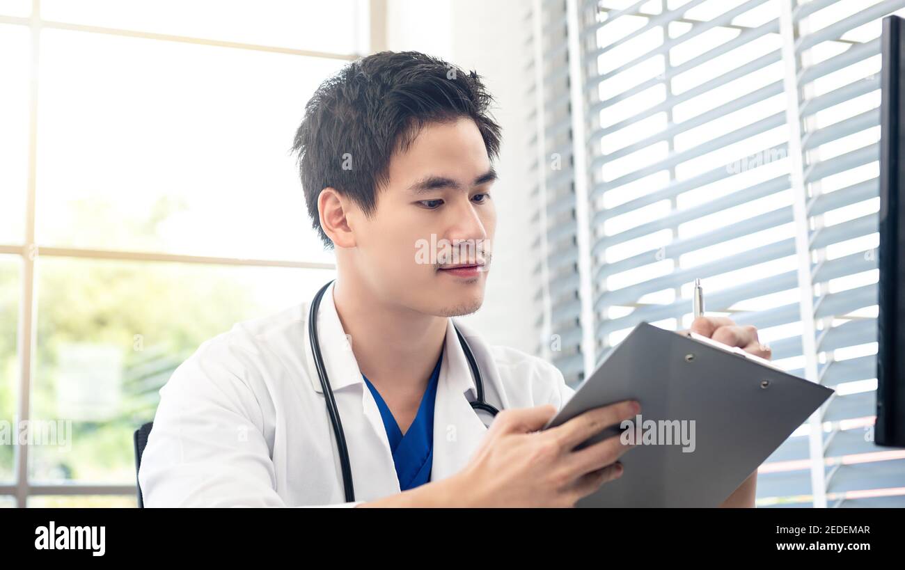 Porträt eines jungen attraktiven männlichen asiatischen Arzt gehen durch seine medizinische Liste in seinem Büro. Stockfoto