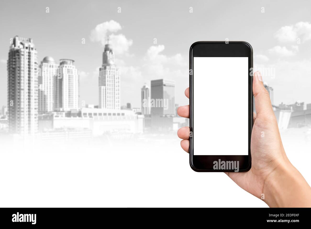 Hand hält Smartphone mit leerem Bildschirm und Stadtgebäude im Hintergrund, Immobilien-Anwendungskonzept Stockfoto