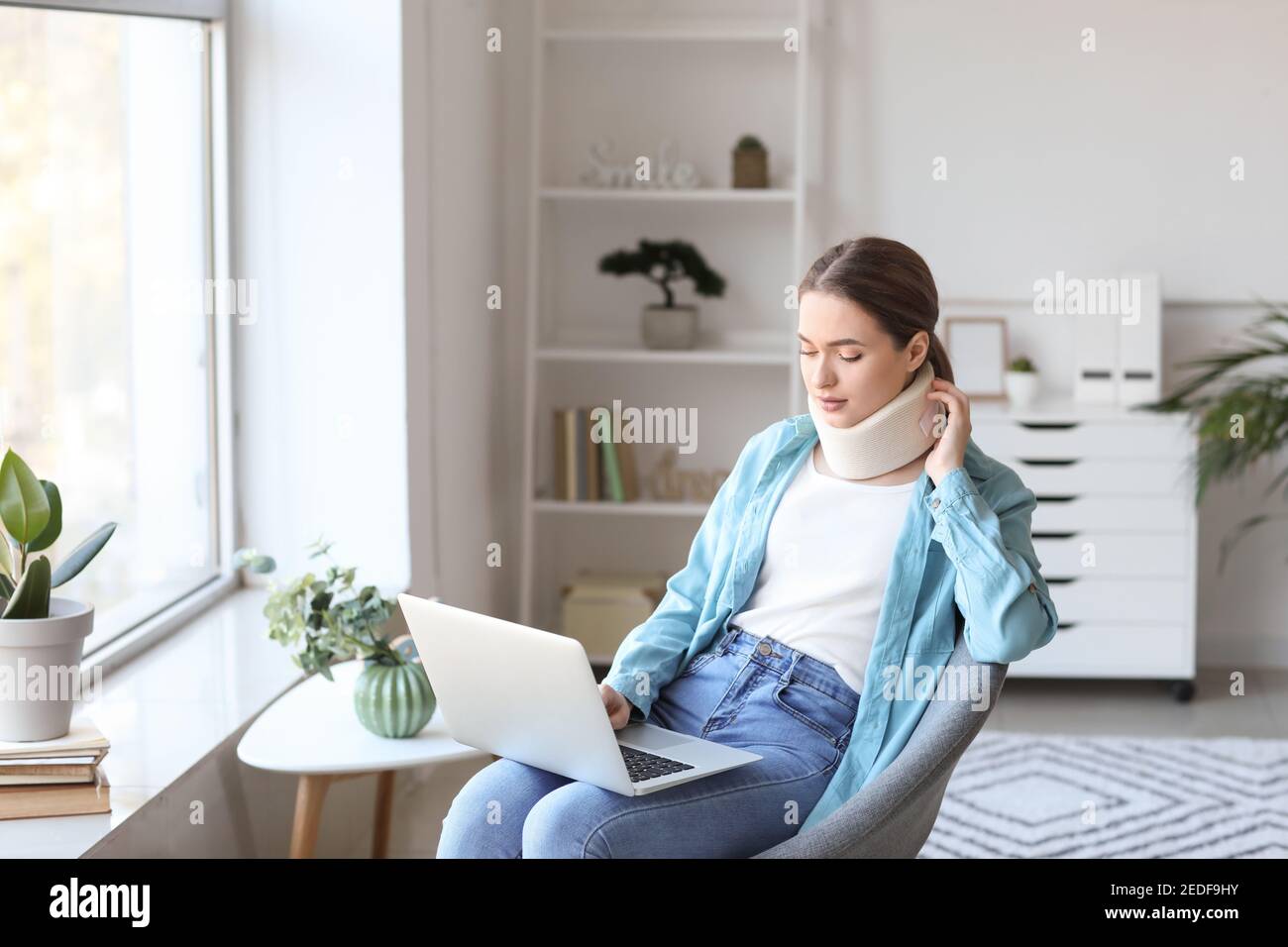 Junge Frau mit Halsband am Hals mit Laptop an Zu Hause Stockfoto