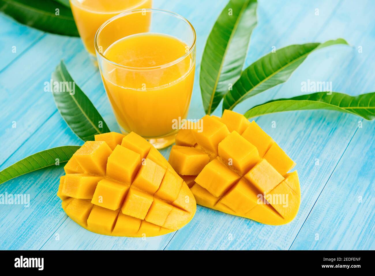 Erfrischende Getränke für den Sommer, kalter süßer und saurer exotischer Mangosaft in den Gläsern auf hellblauem Holztischhintergrund Stockfoto