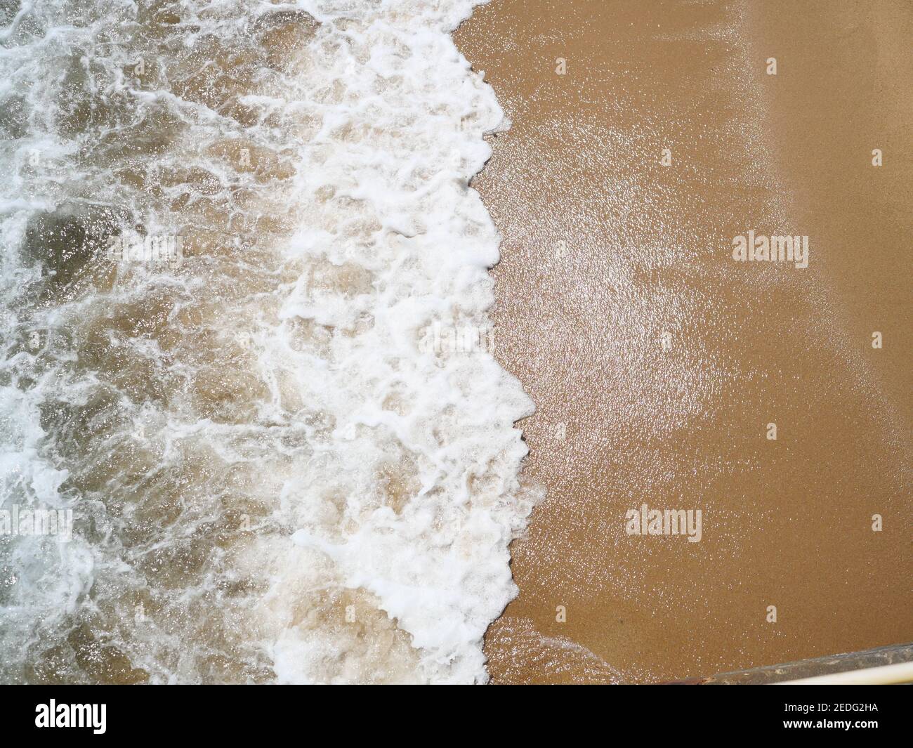 Weiße Blase und grünes Wasser der Meereswelle spritzt auf Brauner Sand des Strandes bei Luftblick Stockfoto