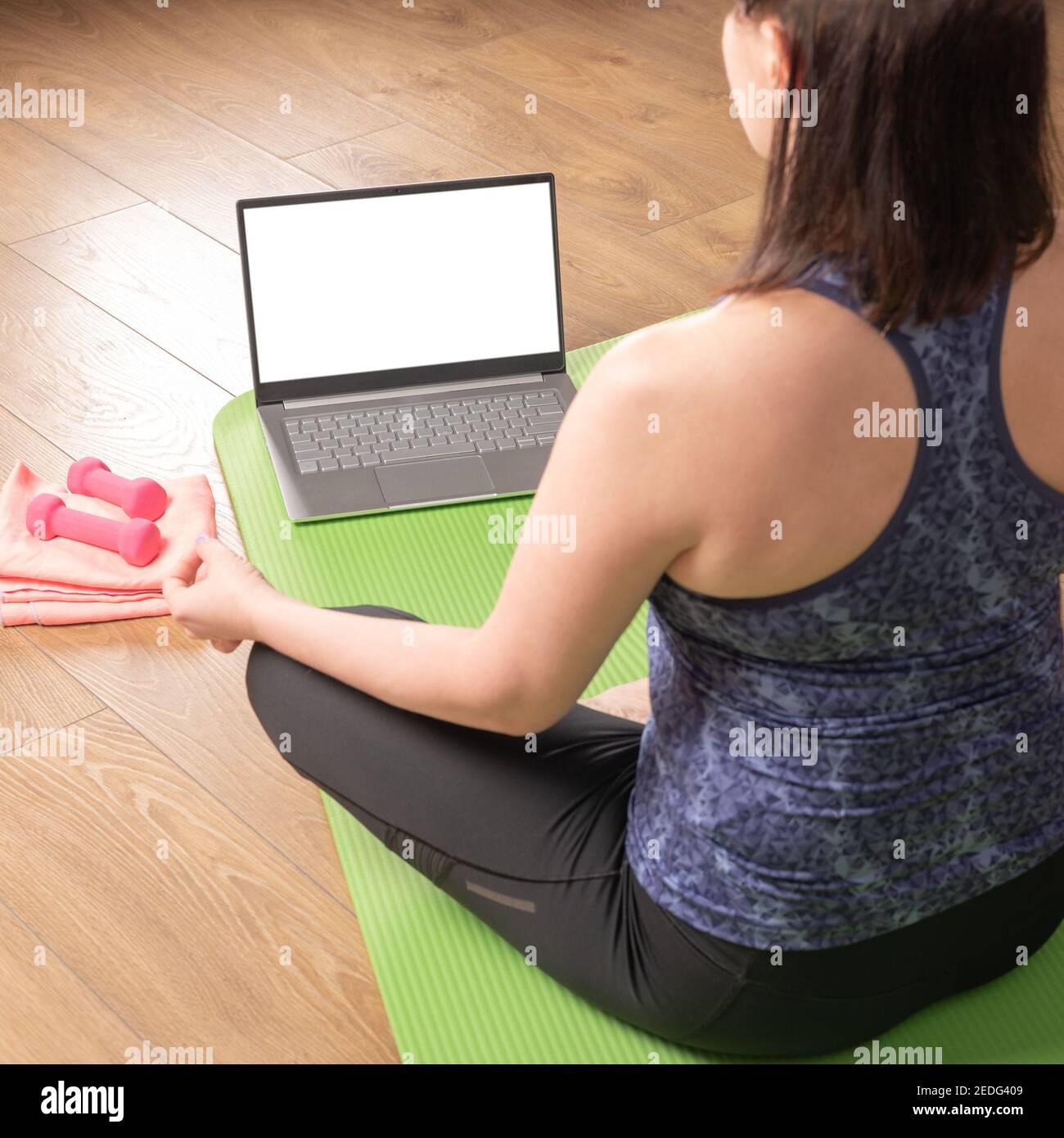 Rückenansicht hinten über der Schulter bei Passform sportlich gesund ruhig Frau sitzt auf der Matte in Lotushaltung und schaut online Yoga Klasse Meditieren Sie Atemübungen auf l Stockfoto