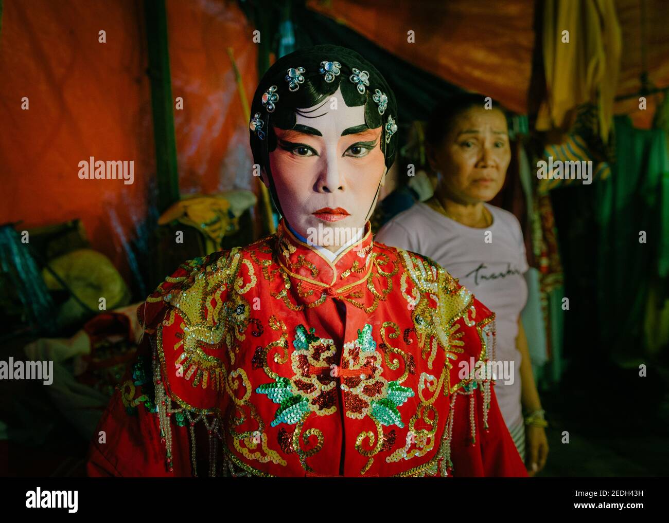 Porträt einer thailändischen chinesischen Opernspielerin hinter der Bühne, trägt ihr buntes Kostüm und Make-up, ihre Kommode ist im Hintergrund. Stockfoto