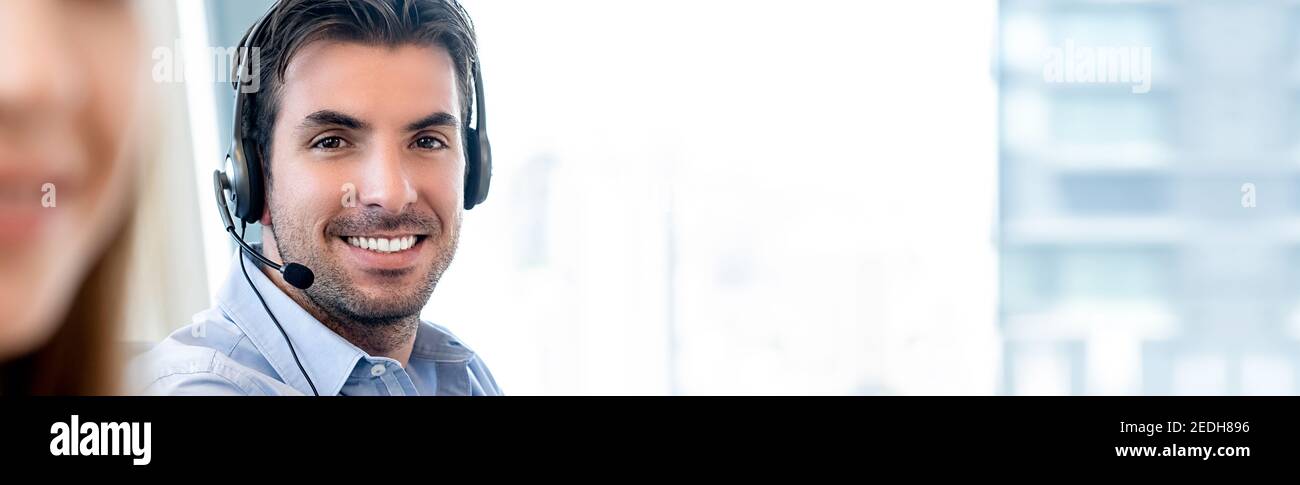 Lächelnder, freundlicher hispanischer Mann, der im Callcenter-Büro arbeitet Ein Telemarketing-Kundendienstmitarbeiter auf Blur-Bannerhintergrund mit Speicherplatz kopieren Stockfoto