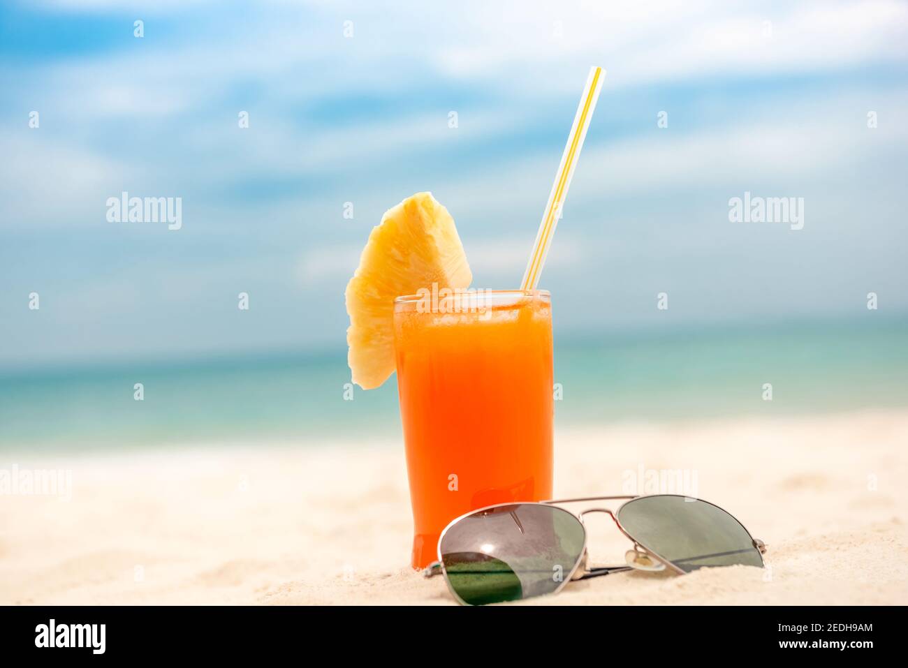 Erfrischendes kaltes Tropenfrucht-Punsch-Getränk mit Sonnenbrille im Sommer Weißer Sandstrand Hintergrund Stockfoto