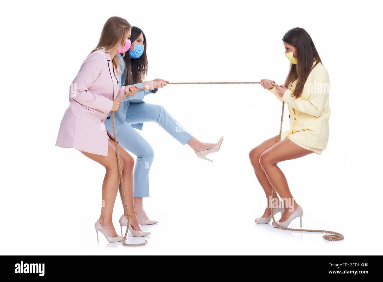 Drei Frauen in Pastellanzügen ziehen Seil über weißen Hintergrund Stockfoto