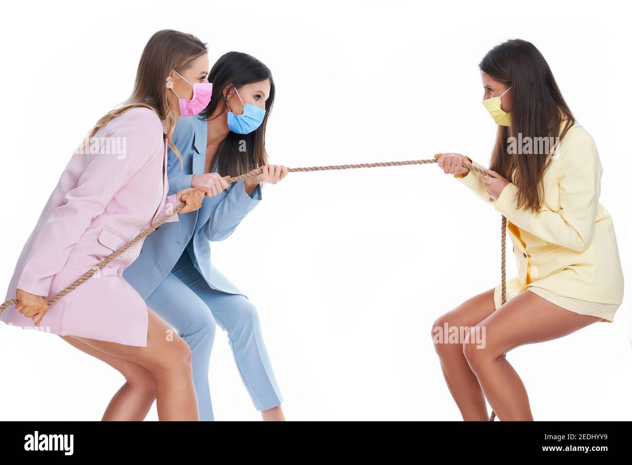 Drei Frauen in Pastellanzügen ziehen Seil über weißen Hintergrund Stockfoto
