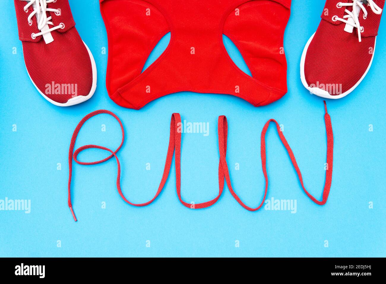 Rote Turnschuhe und ein Trainingstank mit Schriftzug "Run" aus einem Schnürsenkel auf blauem Hintergrund. Kreatives Flat Lay, aktives Lifestyle-Konzept. Stockfoto