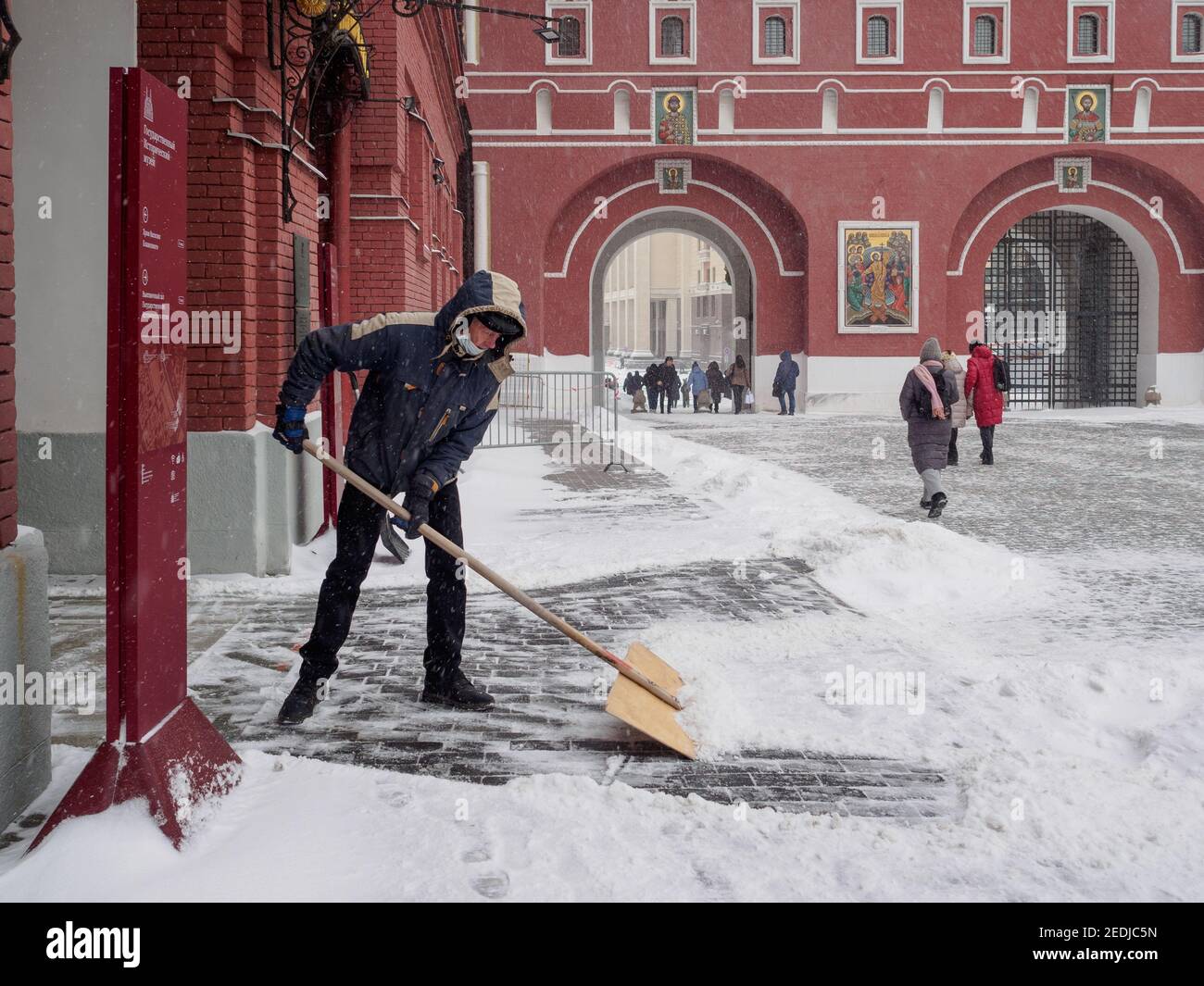 Moskau. Russland. Februar 12, 2021. Ein Mann entfernt Schnee vom Bürgersteig mit einer Holzschaufel während eines Schneesturms an einem Wintertag. Ungewöhnlich schwer Stockfoto