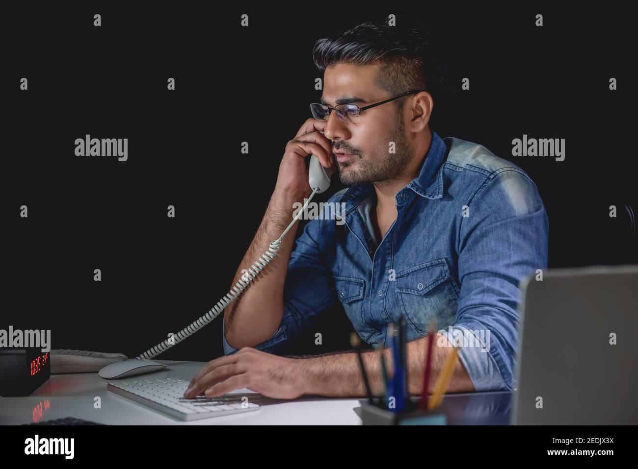 Casual asiatischen Geschäftsmann im Gespräch am Telefon mit Kunden während Überstunden arbeiten spät in der Nacht im Büro Stockfoto